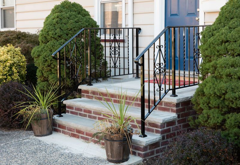 A brick porch with a wrought iron railing and potted plants.