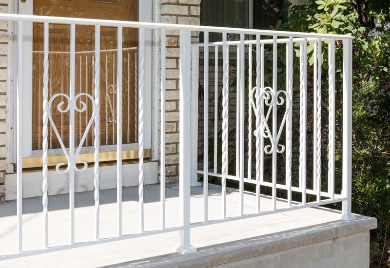 A white railing on a porch with a brick building in the background.