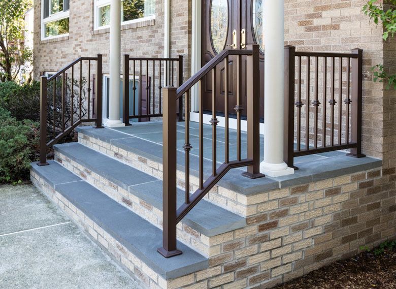 A brick house with a porch and stairs with a wrought iron railing.