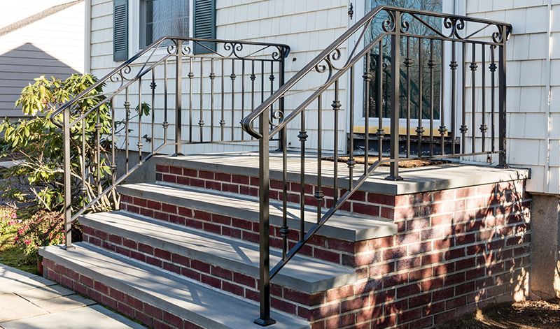 A brick house with stairs and a wrought iron railing.