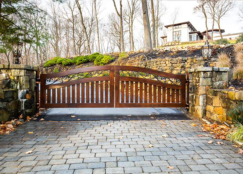 A custom gate is in the middle of a brick driveway.