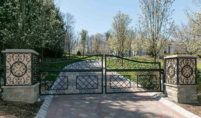 A wrought iron gate surrounds a driveway leading to a house.