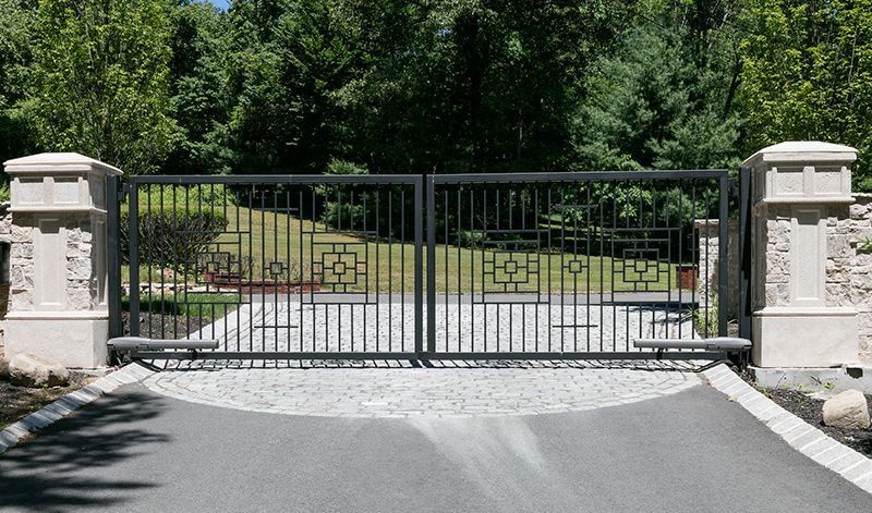 A black gate is open to a driveway with trees in the background