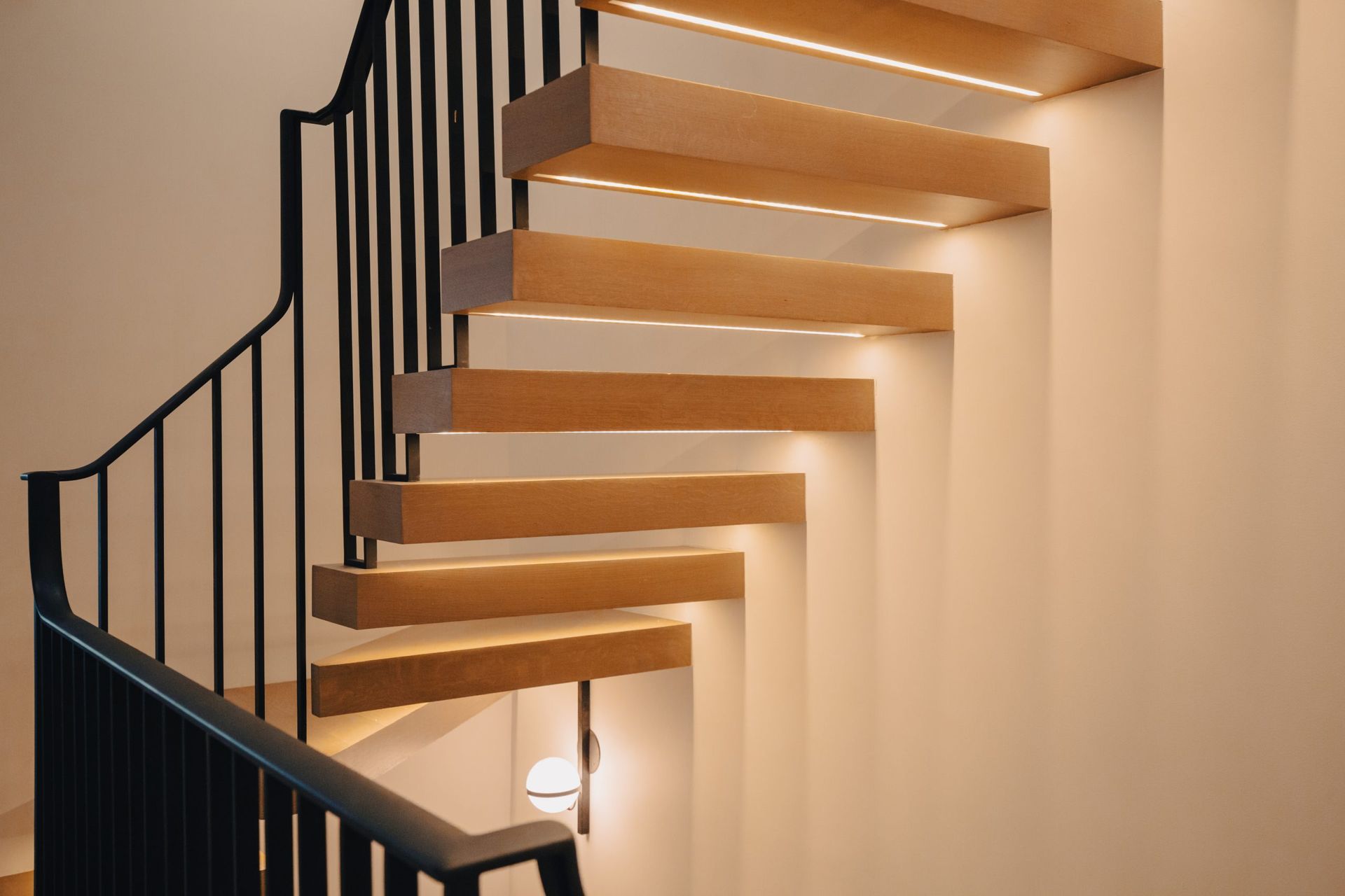 A wooden spiral staircase with a black railing and lights on the steps.