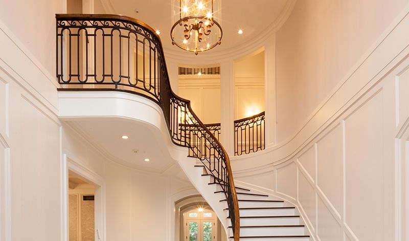 A large curved staircase in a hallway with a chandelier hanging from the ceiling.