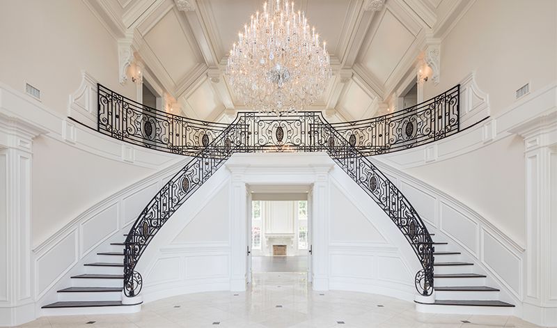 There is a large staircase in the middle of the room with a chandelier hanging from the ceiling.