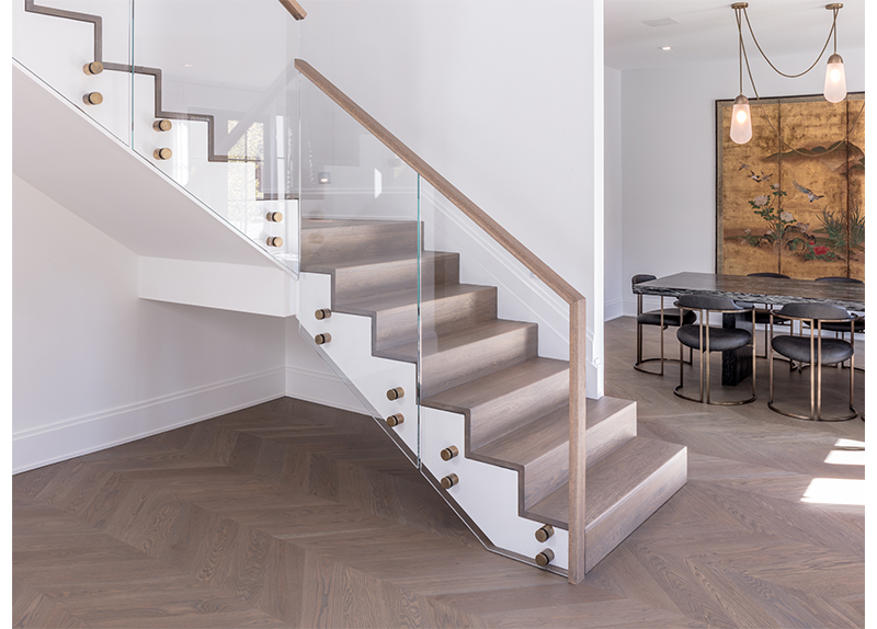 A staircase with a glass railing in a room with a table and chairs.