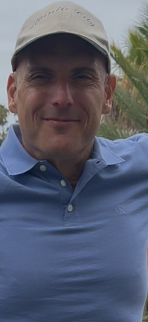 A man wearing a hat and a blue shirt is smiling for the camera.