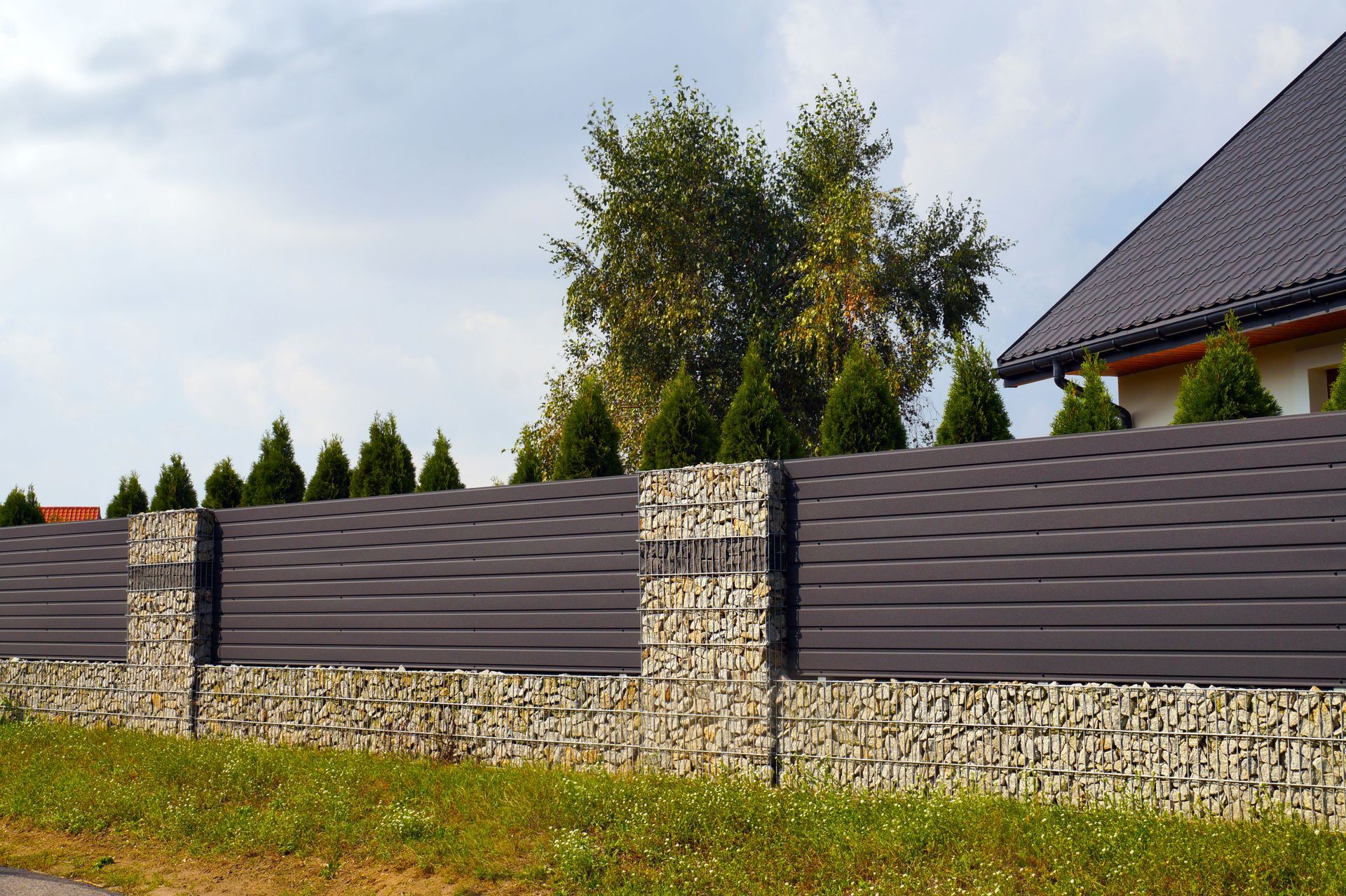 Modern stone and gray wooden fence along a grassy yard beside a house