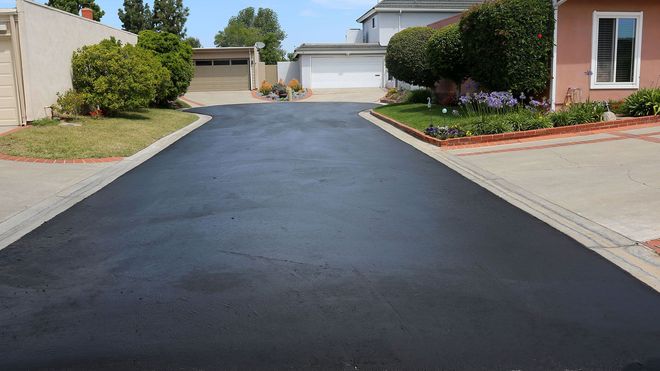 Freshly paved black driveway leading between suburban homes to garages at the end
