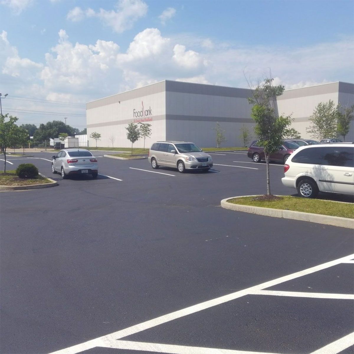 Parking lot outside a beige retail building with a few cars under a blue sky