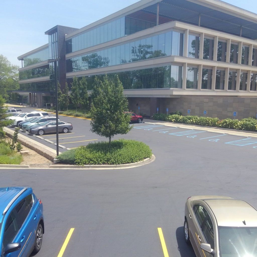 Modern office building with parking lot, cars, and landscaped entrance under clear daylight