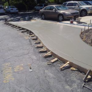 Concrete sidewalk repair along a cracked curb with wooden forms and parked cars nearby