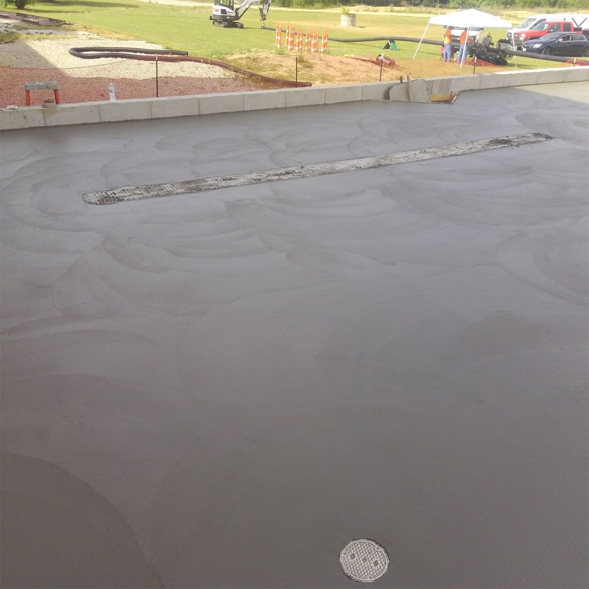 Freshly poured gray concrete slab at a construction site, with a curb and grassy park in the background