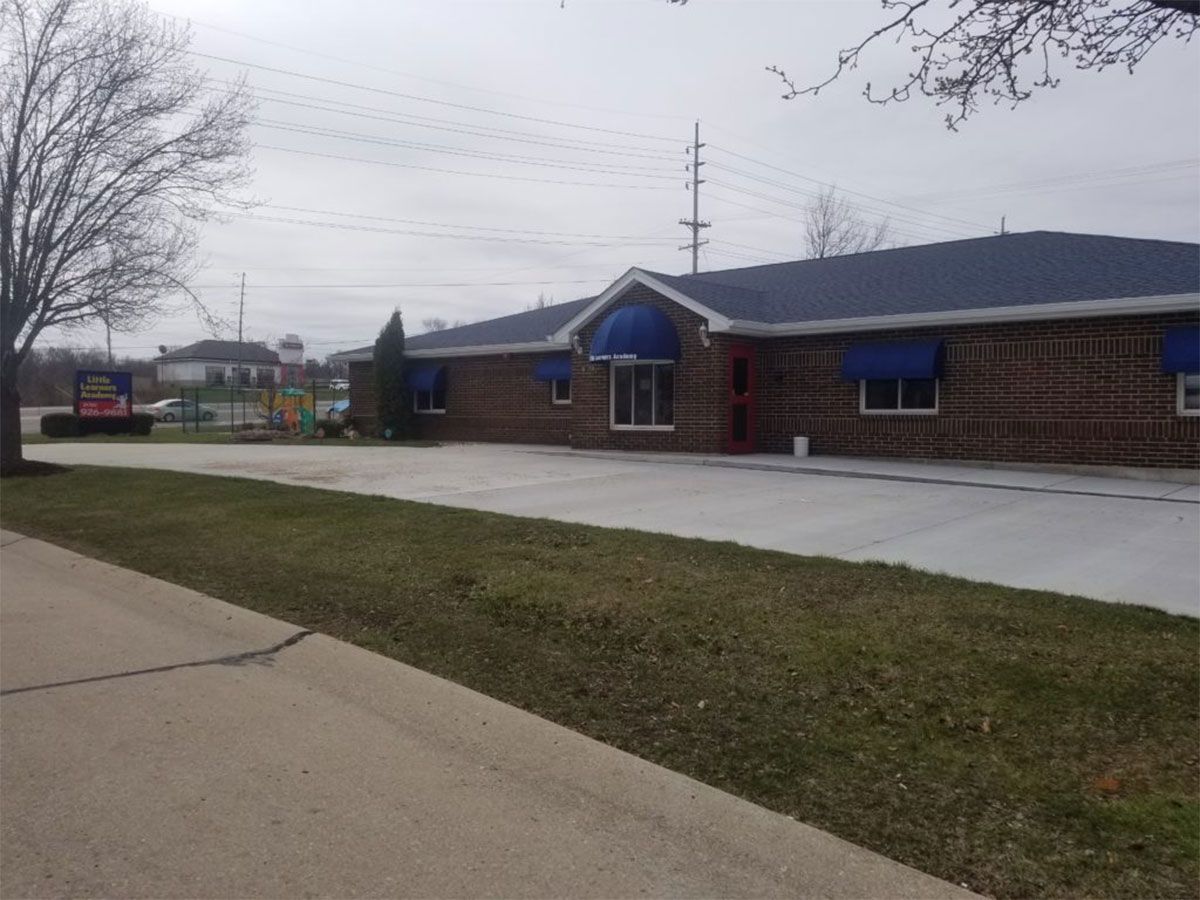 Single-story brick building with blue awnings and a sidewalk on an overcast day