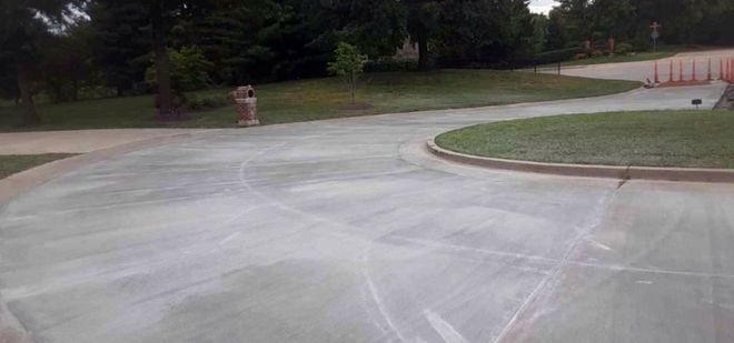 Empty paved driveway curving past a grassy park area with trees and a picnic table.