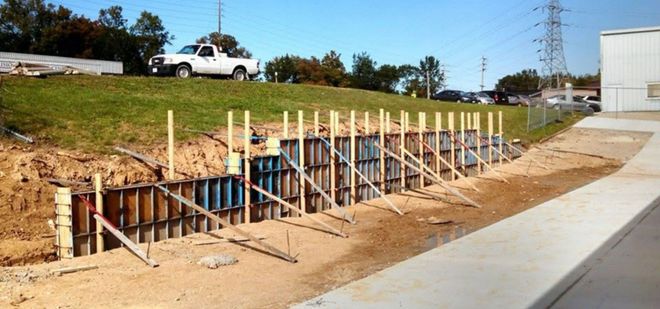 Roadside construction trench with wooden supports beside a sidewalk and grassy slope