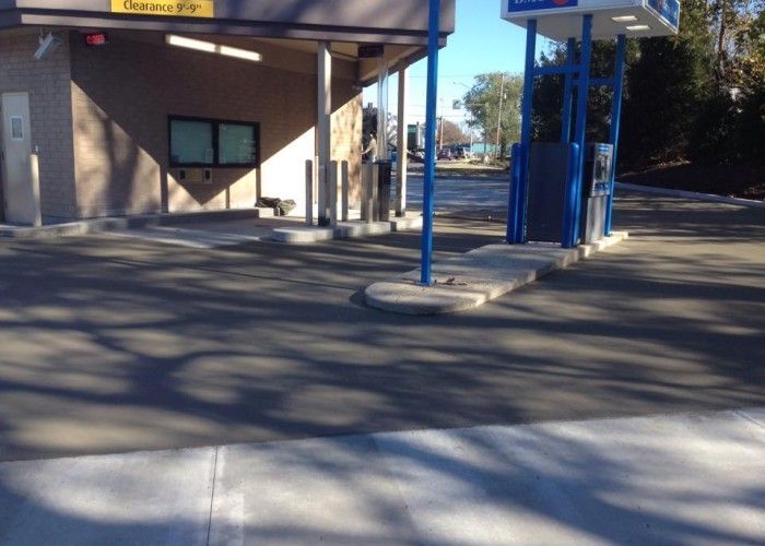 Blue bus stop shelter beside a building, with a paved area and long tree shadows.