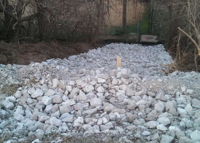 Rocky riverbed or construction site with a large pile of light gray stones and a yellow marker in the center