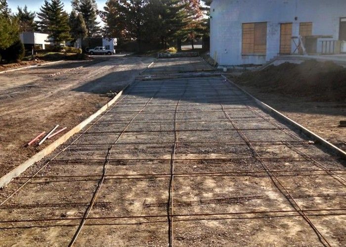 Freshly poured concrete driveway in front of a house, with construction lines and tools on the left.