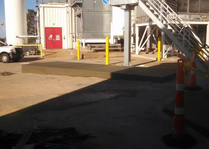 Industrial yard with white containers, red doors, yellow bollards, and stairs in sunlight and shadow