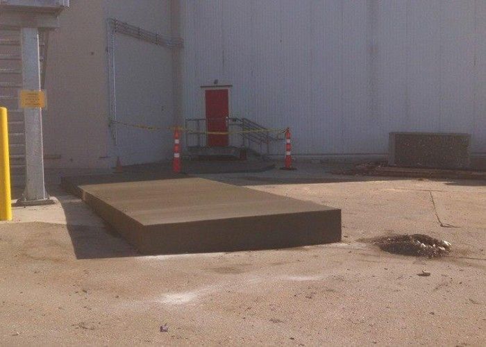 Loading dock with a low concrete platform, orange cones, and a red door against a white wall