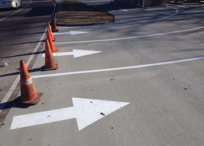 Traffic cones and white directional arrows painted on a paved road.