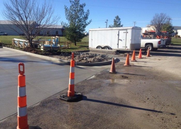 Roadwork area with orange traffic cones, a white trailer, and a pickup truck beside a paved road