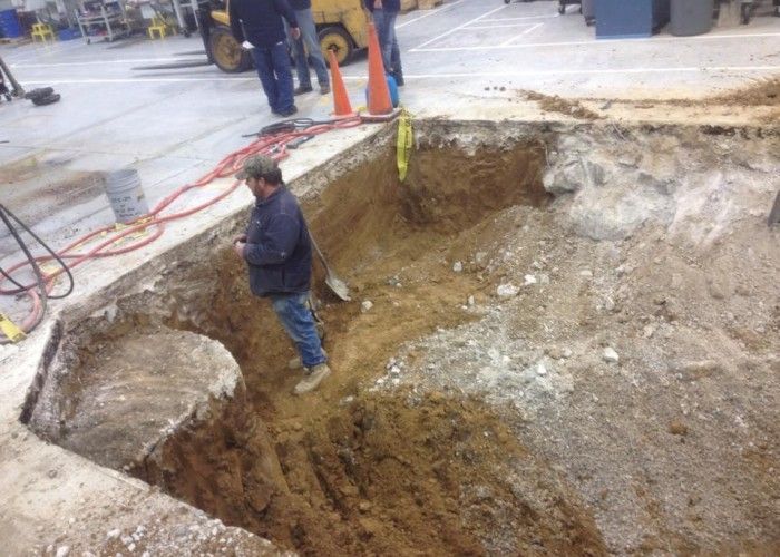Worker standing in a large construction excavation beside a concrete floor, with safety ropes and equipment nearby