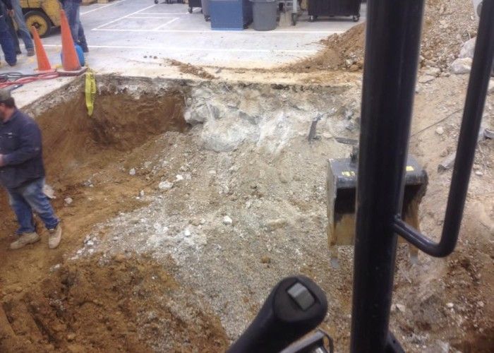 Construction site with a large excavated hole, dirt mound, and a worker standing at the edge.