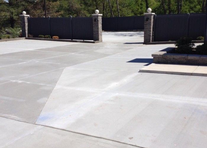 Concrete driveway entrance with black gates and landscaped planter walls.