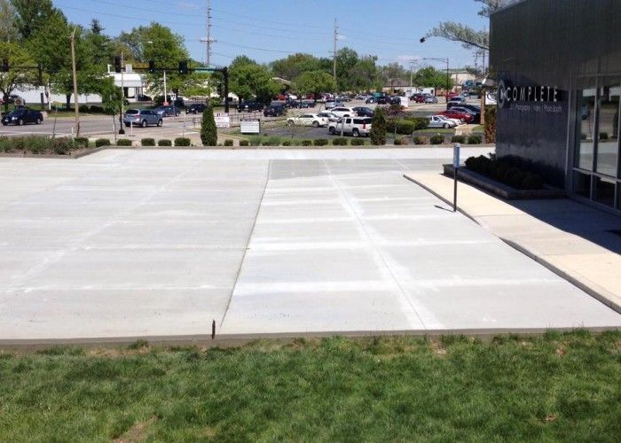 Empty concrete sidewalk area beside a building, facing a parking lot on a sunny day