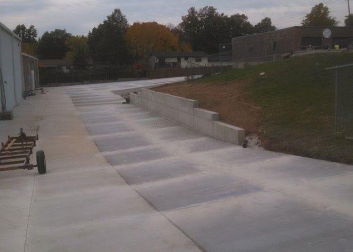 Concrete walkway with wide steps and ramps beside a building on a sloped outdoor campus.