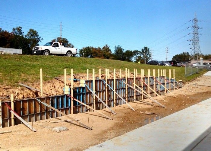 Roadside concrete formwork and rebar trench under construction beside a grassy slope and parked white truck