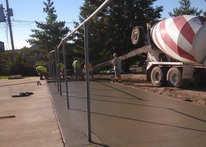Workers smoothing a concrete sidewalk beside a red-and-white cement mixer truck