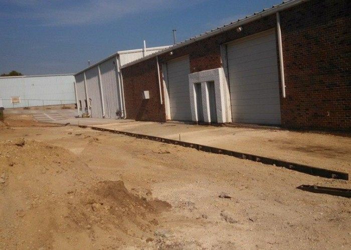 Industrial warehouse building with brick and metal siding on a dirt lot under a clear sky