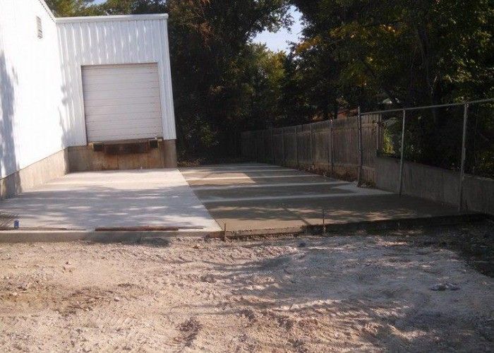 Empty concrete driveway beside a white building and chain-link fence, with a loading dock in back.