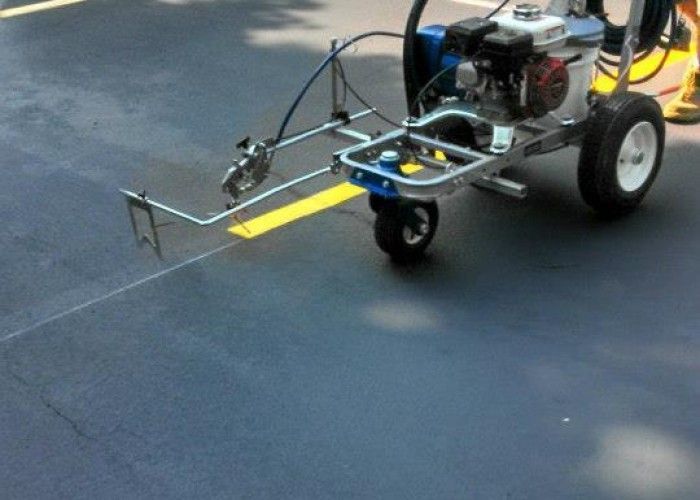 Small wheeled machine spraying liquid on a dark pavement surface outdoors