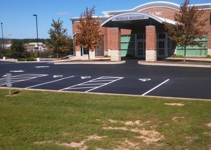 Empty parking lot in front of a brick building with a white arched entrance and trees.