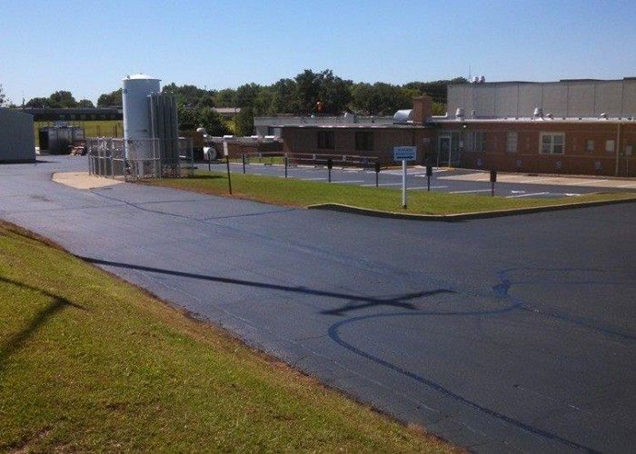 Industrial facility with a paved lot, grass verge, tanks, and low brick buildings under a clear sky