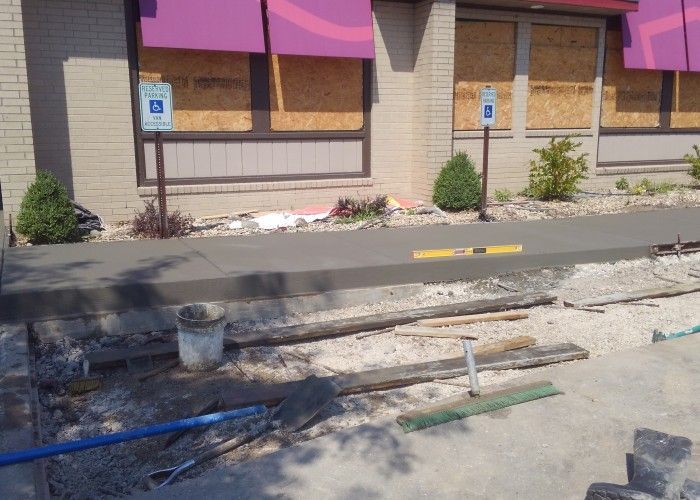 Sidewalk construction trench in front of a storefront with yellow caution tape and wheelchair parking signs.
