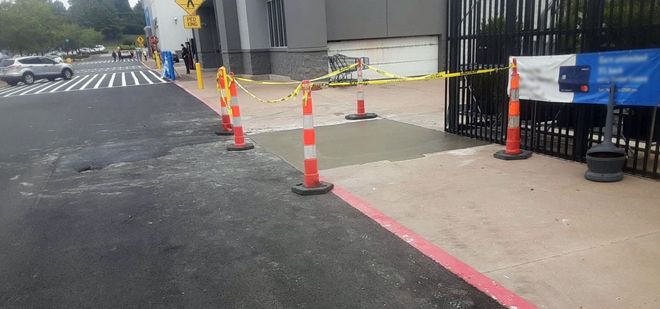 Orange cones and caution tape block a sidewalk beside a street and building entrance