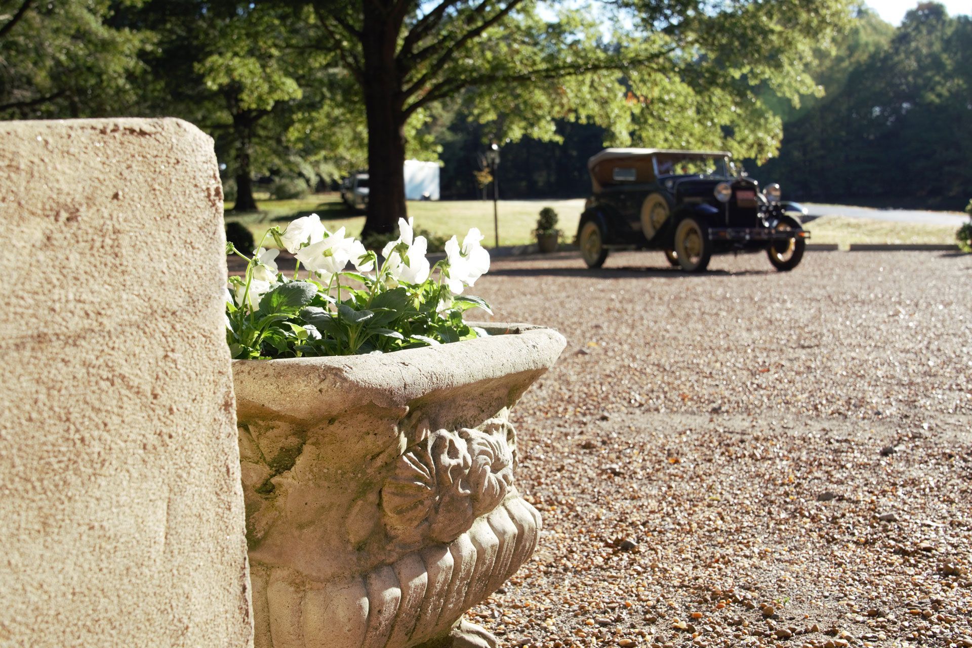 an antique car is parked on a gravel driveway behind a stone planter