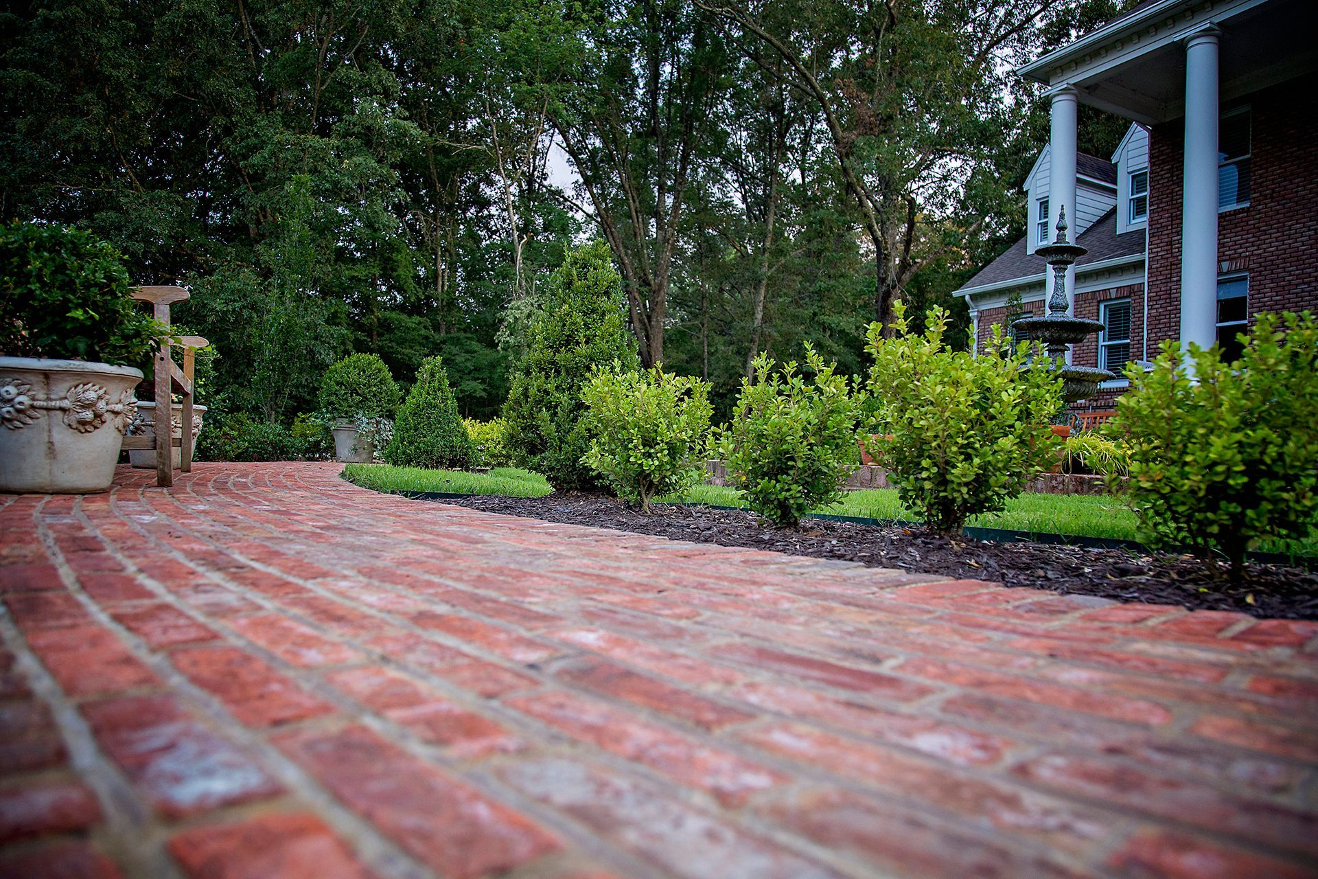 a brick walkway leading to a house with trees in the background .