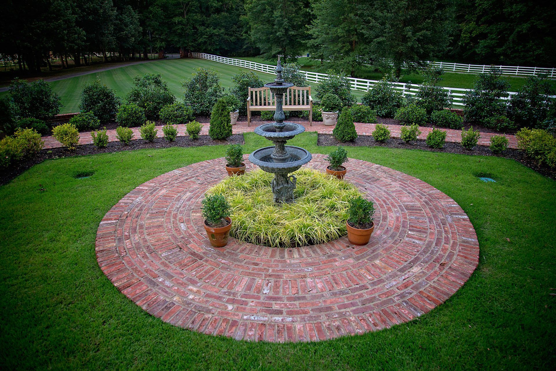 a fountain is in the middle of a brick circle in a garden .