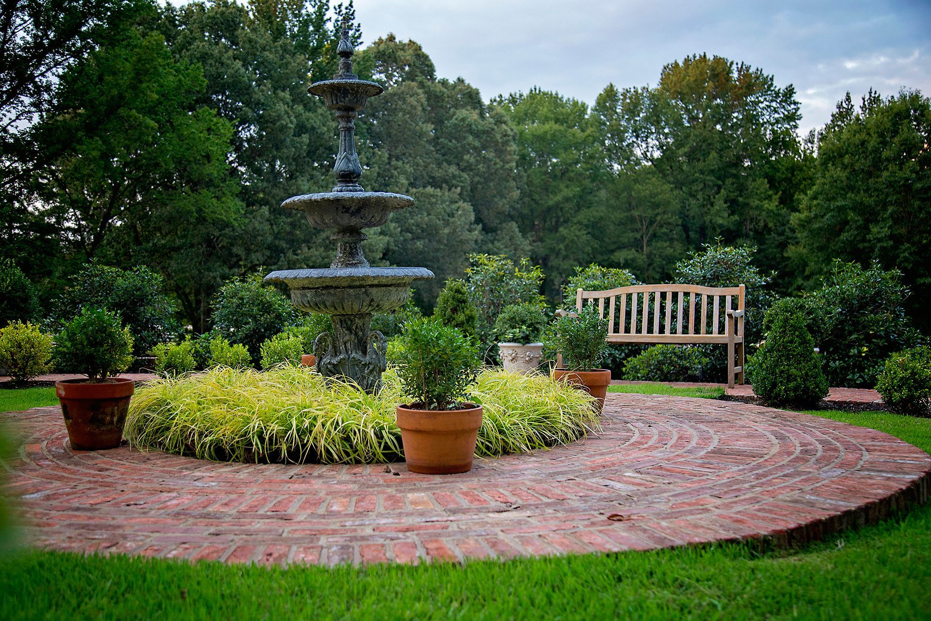 a brick walkway around a fountain and a bench in the background