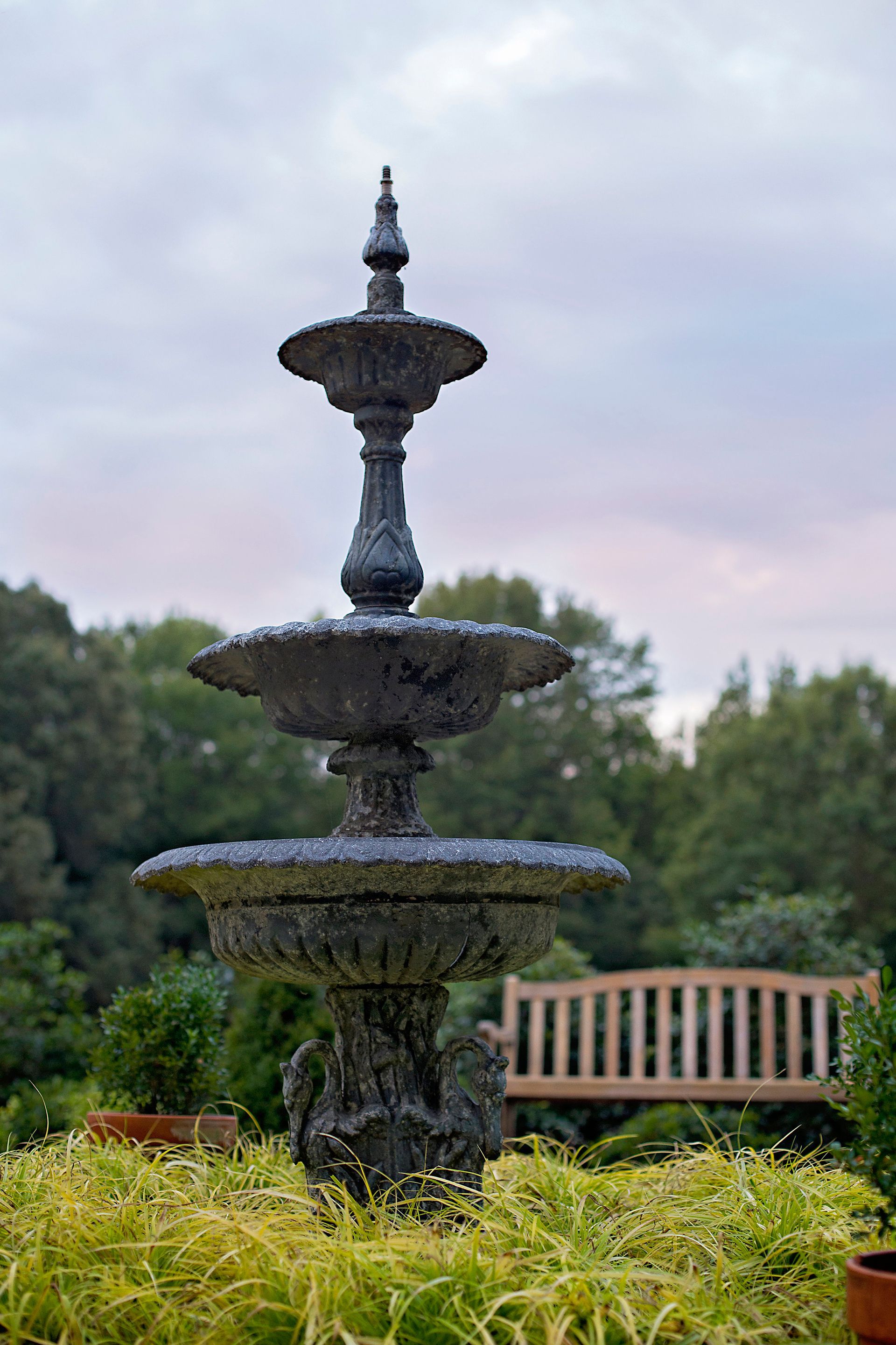 a large fountain in the middle of a garden next to a wooden bench .