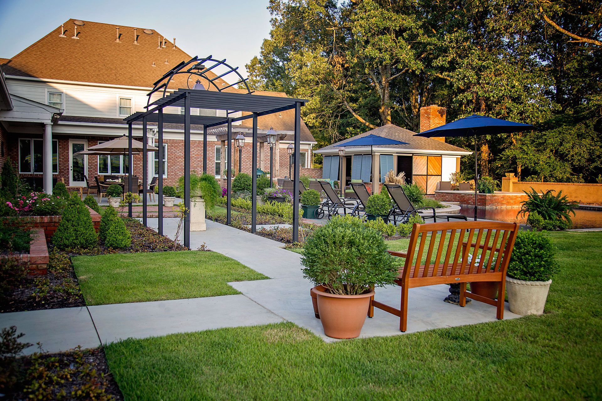 a lawn with a bench and umbrellas in front of a house