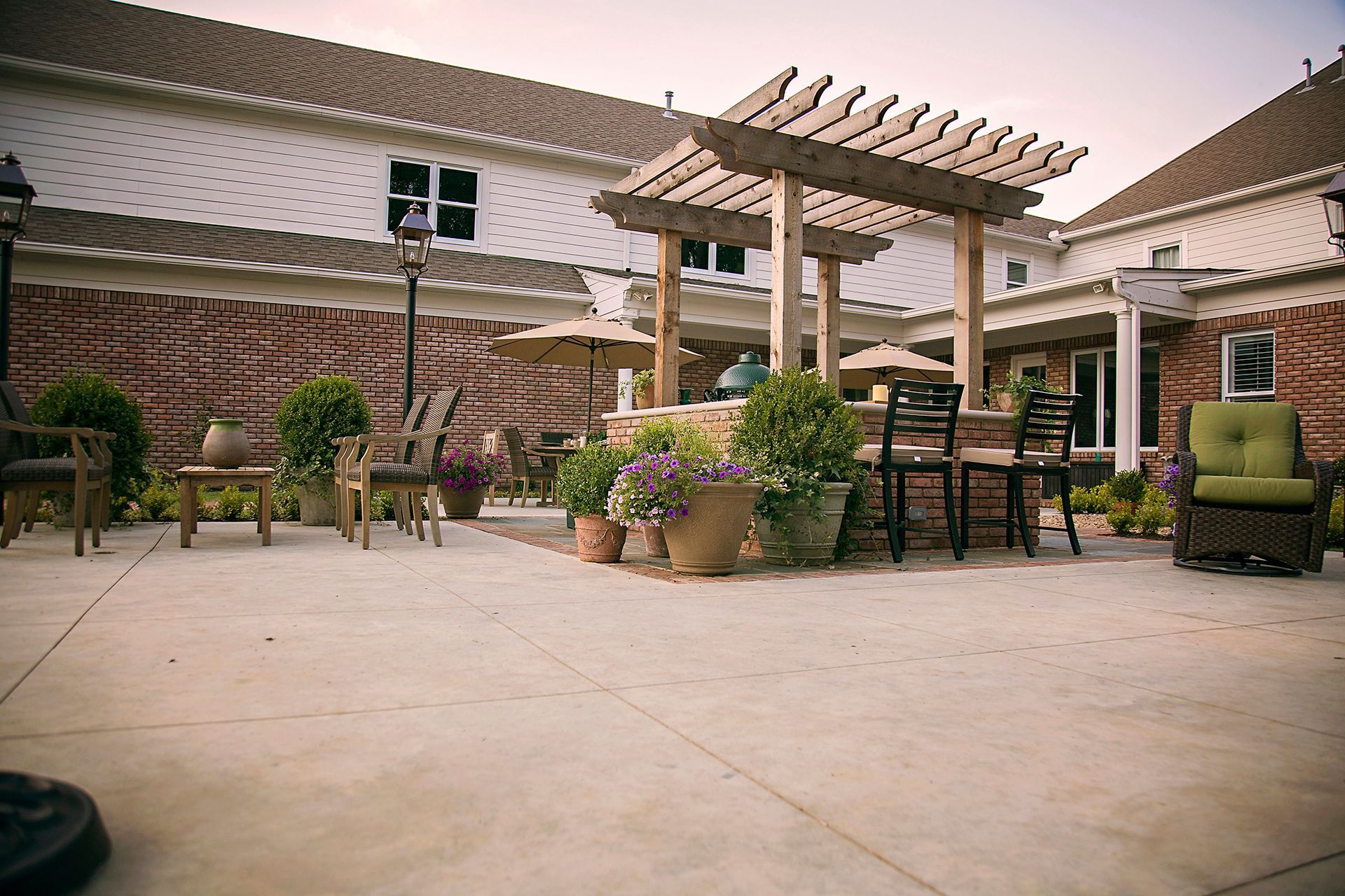 a patio with a pergola , chairs , tables and umbrellas in front of a house .