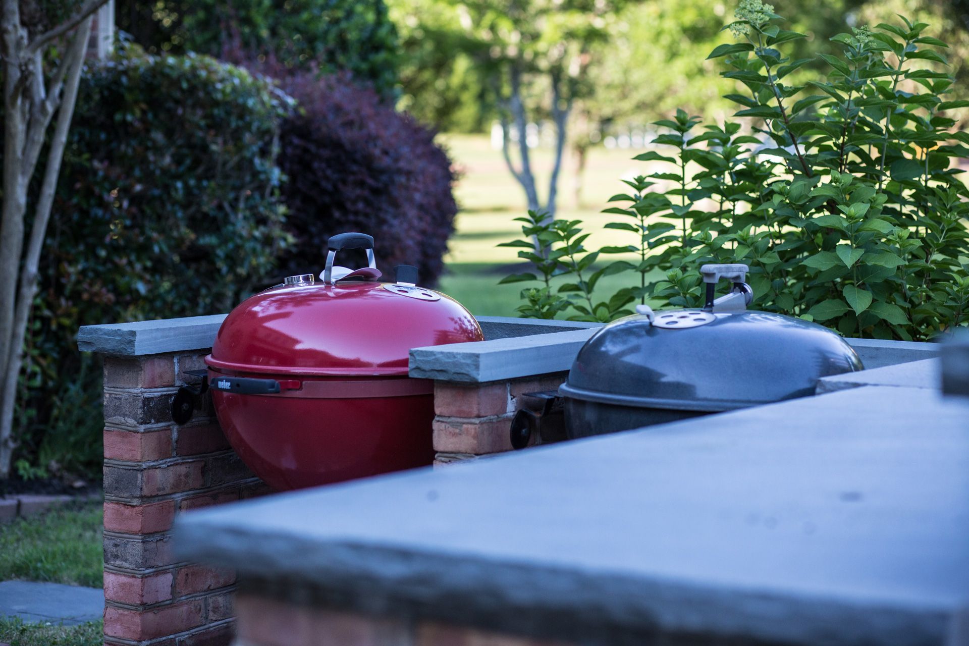 red and black grills are sitting next to a brick counter on a patio.